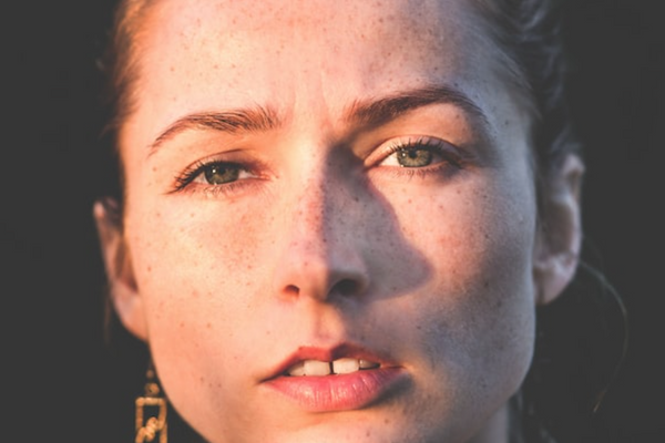 Woman with freckles and green eyes, not smiling, wearing natural-colored lipstick from a clean beauty brand.