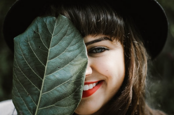 A woman with dark hair smiling and holding a leaf up to her face while wearing the best clean lipstick.