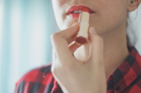 A pale woman applies vivid red antioxidant lipstick