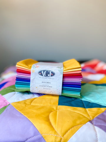 Bundle of fabric in rainbow colors on top of a colorful quilt