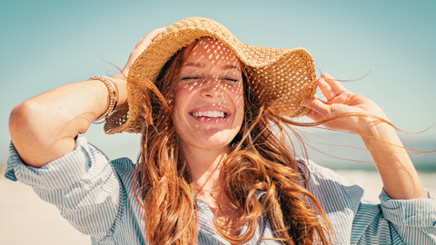 This is a photo of a woman wearing a sun hat, protecting both her hair and her face, while at the beach. This photo is used in the Ippodaro Natural Salon blog post titled, “Mastering Summer Hair Care: Top Tips for Healthy Hair”