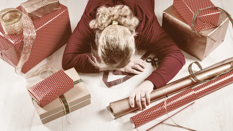 A woman laying face down surrounded by christmas presents and wrapping paper. This image is used in the Ippodaro Natural Salon blog post titled, “Stress-Free Holidays: Prevent Hair Loss and Maintain Gorgeous Locks”.