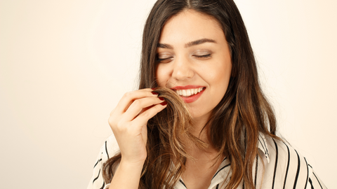 This is an image of a beautiful, long-haired brunette, smiling while holding a chunk of her hair up towards her face. This image is used in the Ippodaro Natural Salon blog post titled, “If You Want Luxurious Hair, You CAN NOT Overlook an Oily Scalp”.