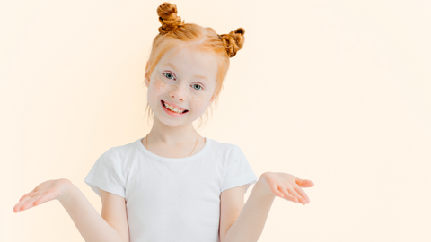 This is an image of a young, female, redhead sporting braided pigtails, posing with her hands as though she is asking a questions. This image is used in the Ippodarro Natural Salon Blog Post titled, “There are So Many Hairstyles for Kids! Here are Some Ideas, Tips, and Tricks for the 2023 School Season!