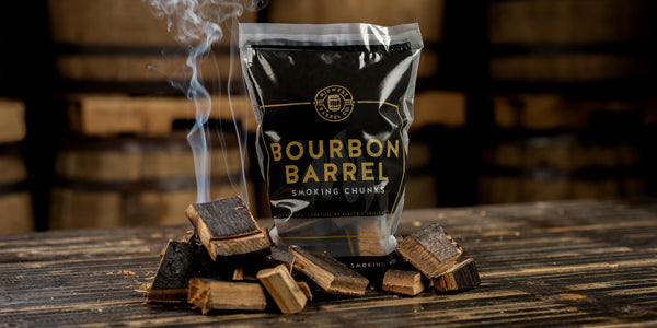 A bag of bourbon barrel smoking wood chunks by Midwest Barrel Co. next to a small pile of chunks that are smoking