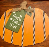A green wood tag with "Happy Fall, Y'all" painted on it. The tag is attached just left of center on the pumpkin.