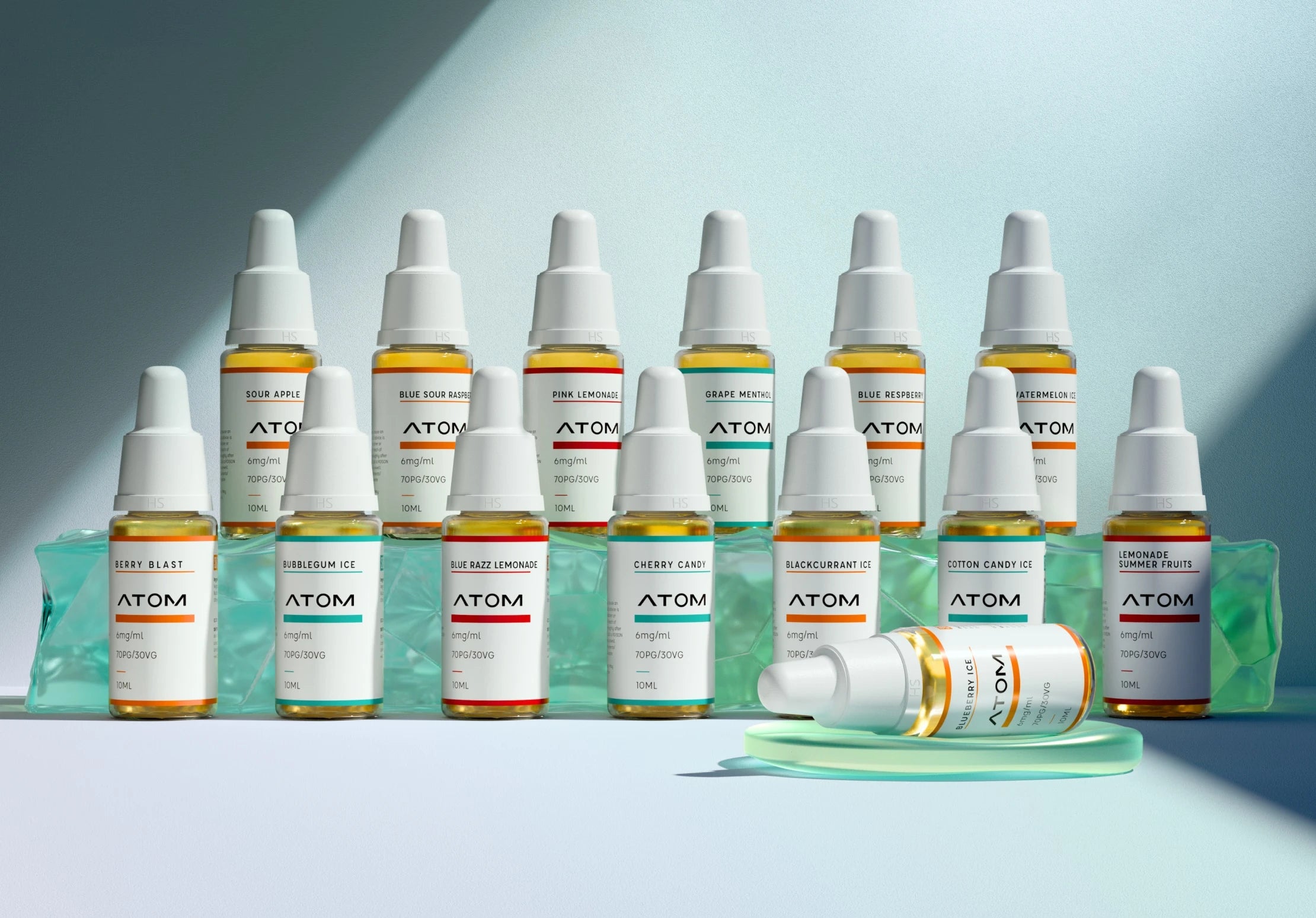 A collection of Hangsen Atom brand e-liquids in various flavors, each with a color-coded label to match the flavor, arranged in two neat rows on a light surface. One bottle lies horizontally in the foreground on a translucent green object.
