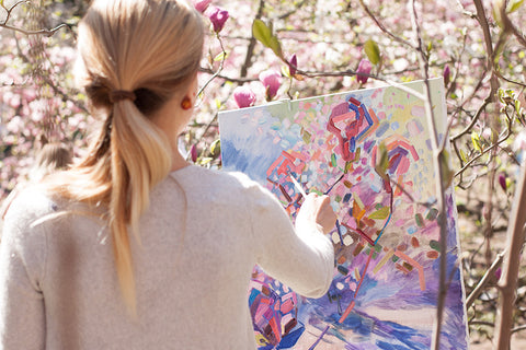 A female artist painting an image on a canvas in a sunny outdoor setting