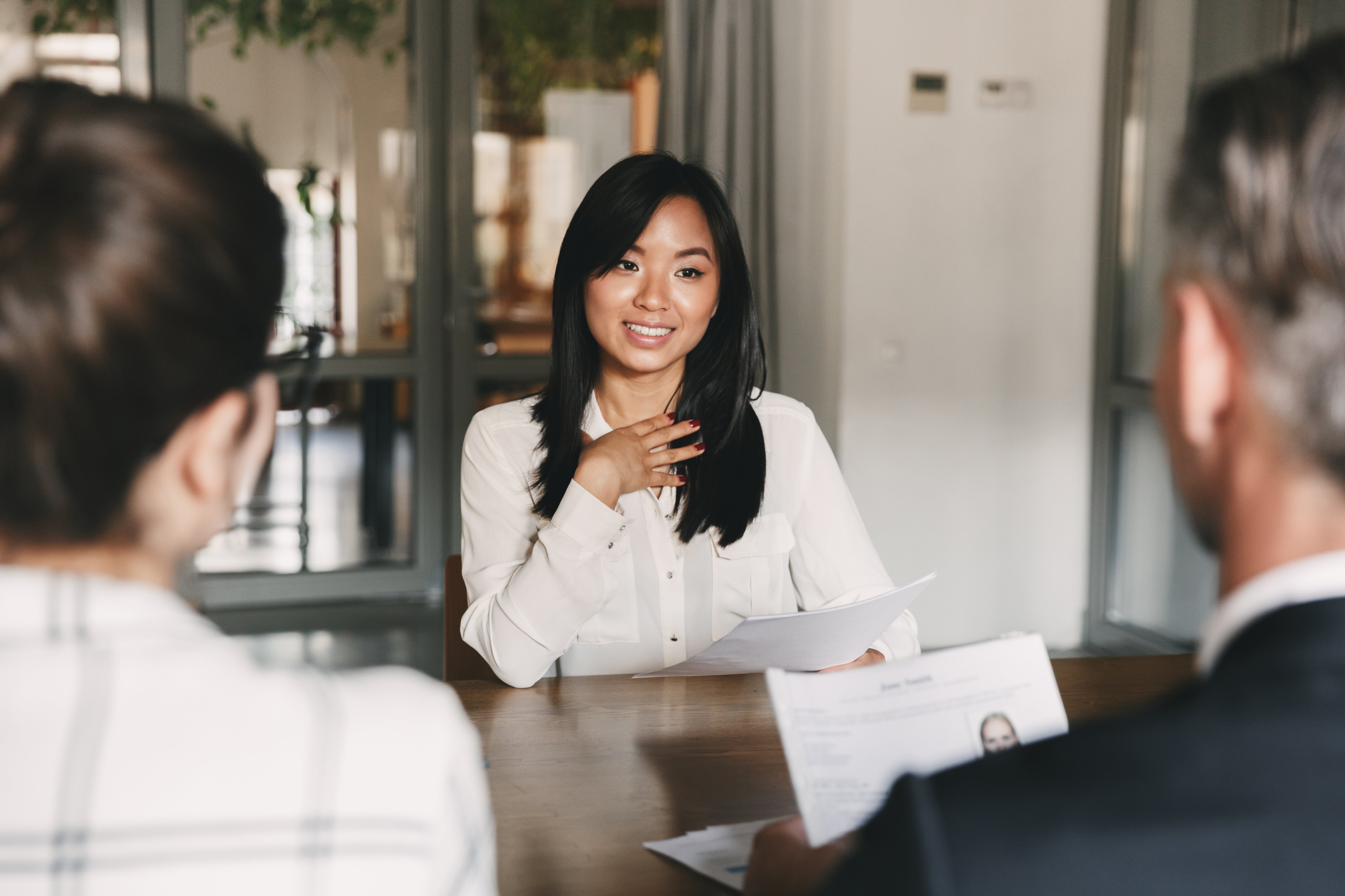 A woman in a white blouse during a job interview with two interviewers.