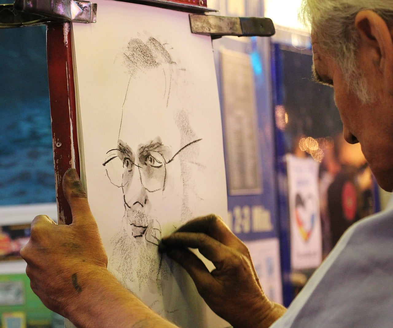 Artist using charcoal to paint a man's face wearing glasses