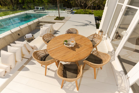 Scenic view of a Grace Recycled Teak Dining Setting featuring Monsoon Wicker chairs with Teak legs, arranged on a deck accentuated by white cushions, overlooking a sparkling swimming pool.