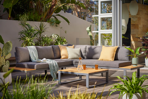 Alpha Outdoor Aluminium Lounge in Charcoal set against a garden backdrop, with plush cushions, decorative pillows, and a coordinating coffee table.
