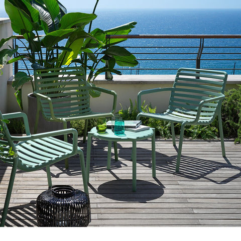 Nardi Doga Outdoor Resin Relax Chair in Agave with a matching table, adorned with a glass and book, set on a wooden balcony adorned with plants and overlooking the sea.