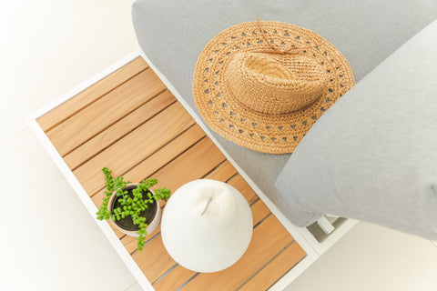 A top-down view of the White Hannover Outdoor Aluminum Modular Lounge with light grey cushions- a modern setup with a side table, adorned with a woven straw hat, small potted plant, and white jar. Effortlessly exudes a relaxed, summery outdoor vibe.