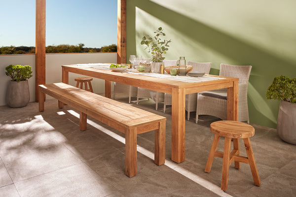 Polly Outdoor Recycled Teak Bench & Dining Table in a natural wood outdoor dining arrangement with Darwin Outdoor wicker dining chairs, simple tableware, greenery, and partial shading for a warm and inviting al fresco atmosphere.