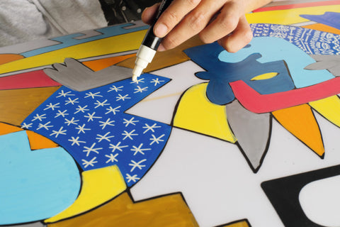 Artist using Posca paint pens on surfboard showing how the paint can be layered
