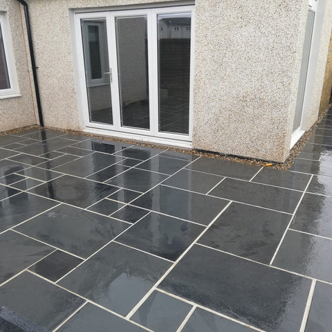 a brazilian blue slate patio installed against the back wall of a house with french doors