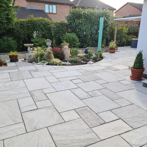 large kandla grey patio with a sunken plant bed in the background. Lots of different plant varities that contrast the grey of the patio