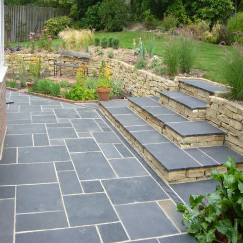 a black limestone patio with steps going up to a lawn level
