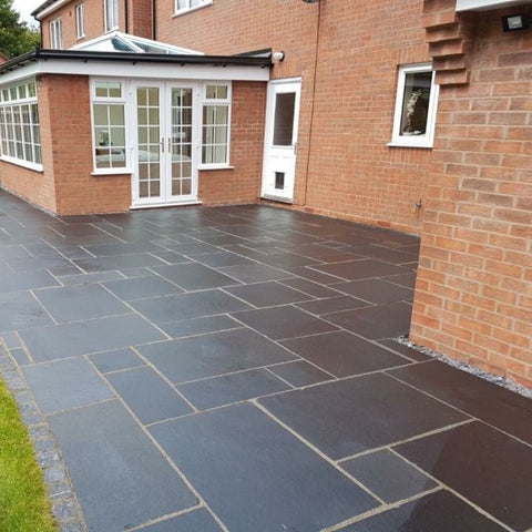 black limestone mixed size patio installed against a redbrick house