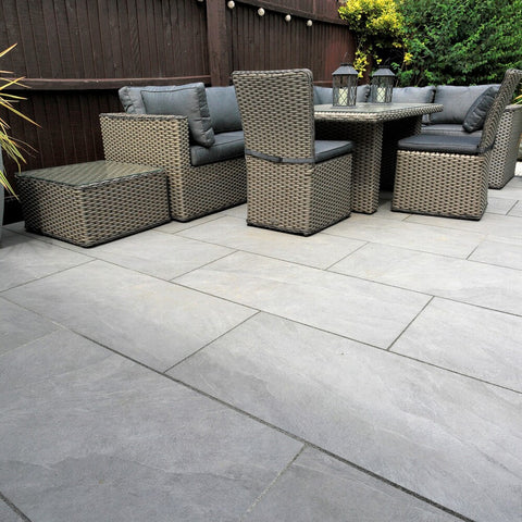 masso grey porcelain paving patio with a rattan furntiure set sat on top of it. Brown fence with small amount of greenery in the background