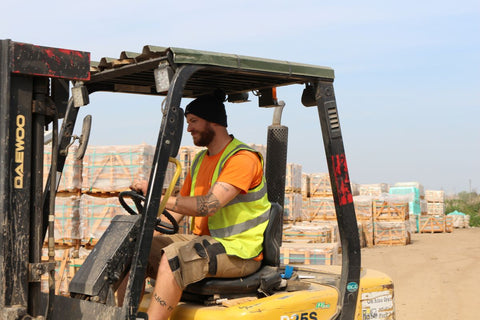 A closer-up shot of our experienced supervisor driving a forklift. The image mainly focuses on him, but the cab of the forklift and some high-quality paving slabs can be seen in the background.