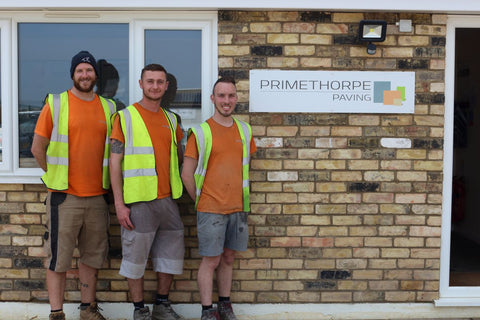 Three dedicated warehouse staff in high-visibility clothing standing in front of the Primethorpe Paving store, ready to fulfill orders of high-quality paving and landscaping materials.