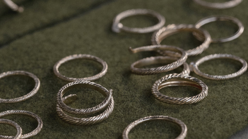 Close-up of a variety of yellow gold Aiden Jae rings with twisted Banyan texture on green wool felt.