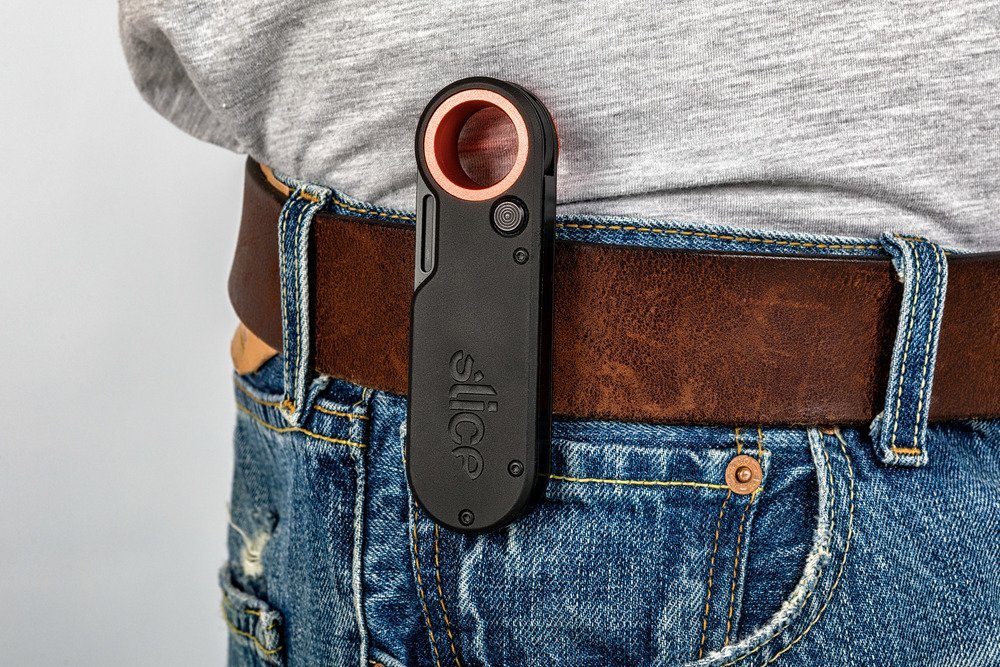 A Slice 10562 Ceramic Folding Knife clipped to the belt of a worker wearing blue denim jeans and a gray tee shirt.