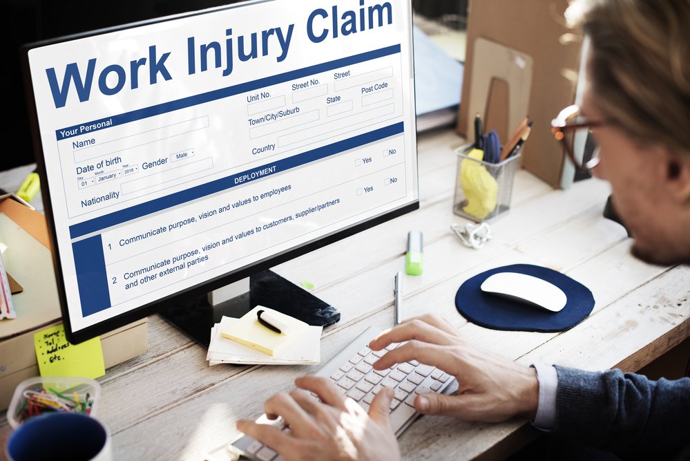 Safety officer sitting at computer screen showing title of “Work Injury Claim” and showing costs of injury on screen