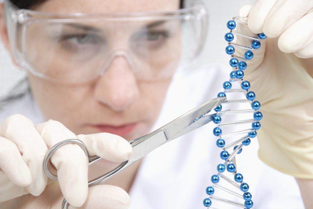 Female lab worker uses lab scissors to cut a blue double helix strand.