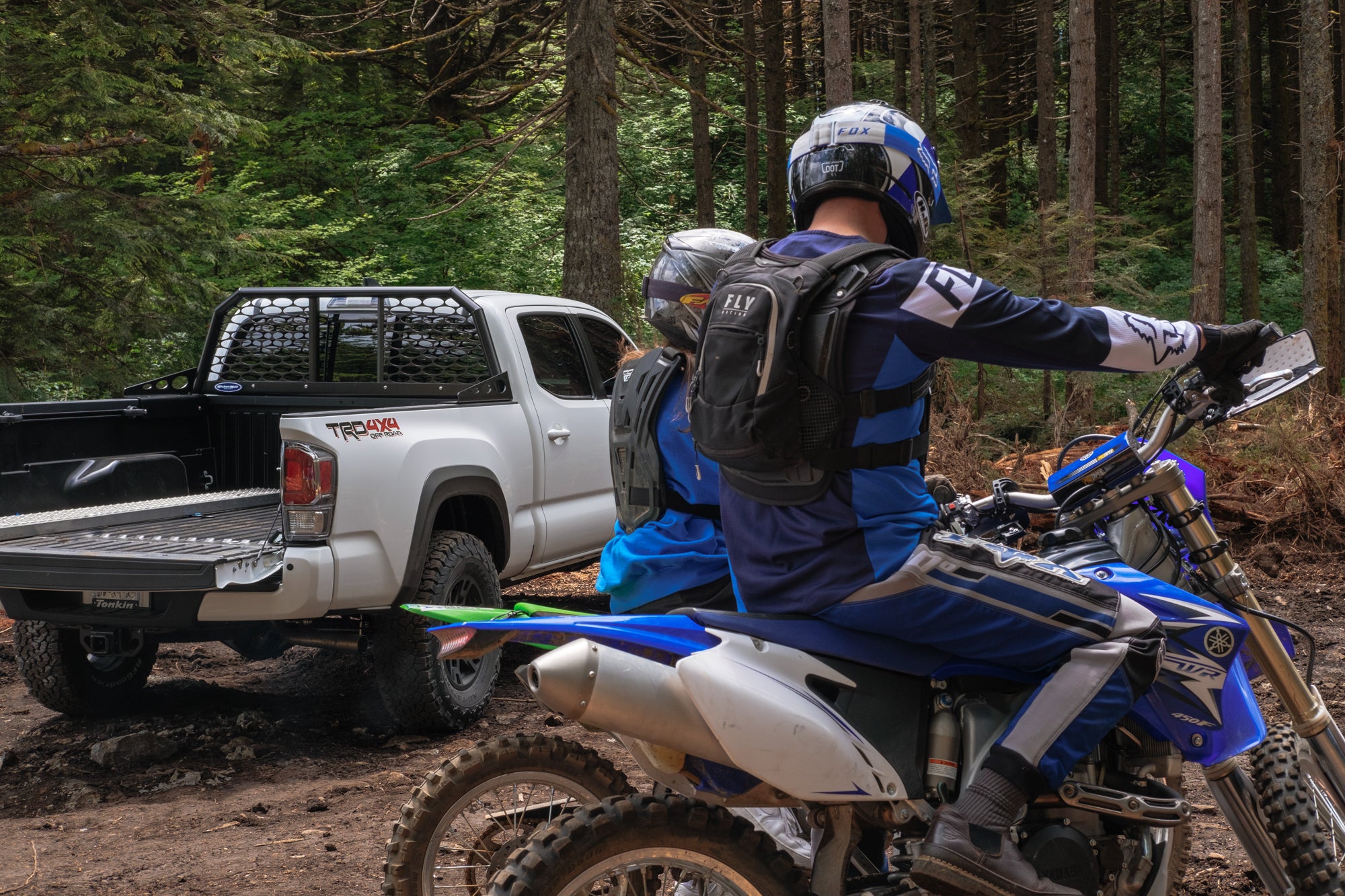 Dirtbikes with riders on them and a truck in the background with a Wickum Rack
