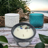 Three candles containing Beach Sea Glass on a wooden table with the beach in the background