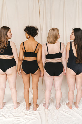 Four women shown from behind dressed in underwear and holding hands