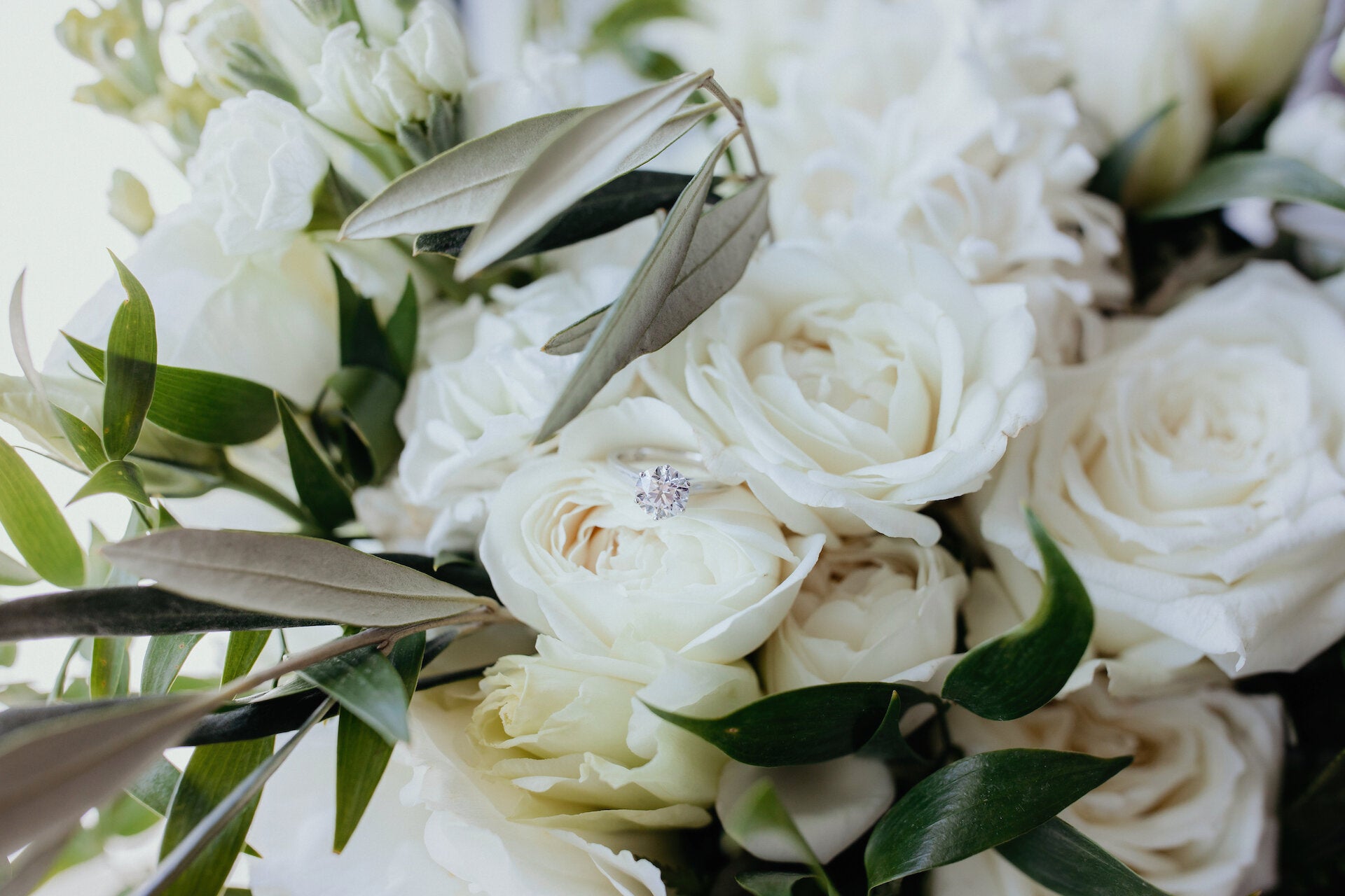 Close up of brides bouquet with white roses and olive branch and diamond engagement ring.