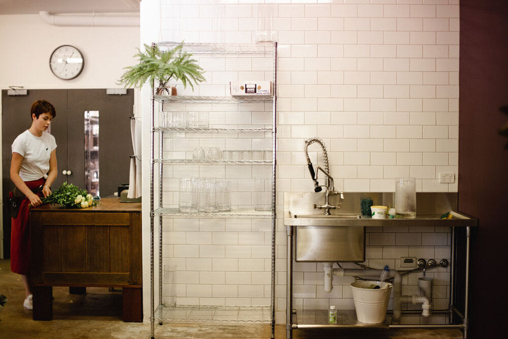 a beija flor florist standing in front of a table near the sink working on flower arrangement