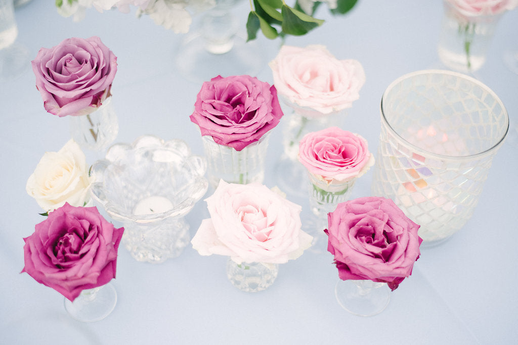 a bunch of pink and white flowers in vases and assorted transparent vases