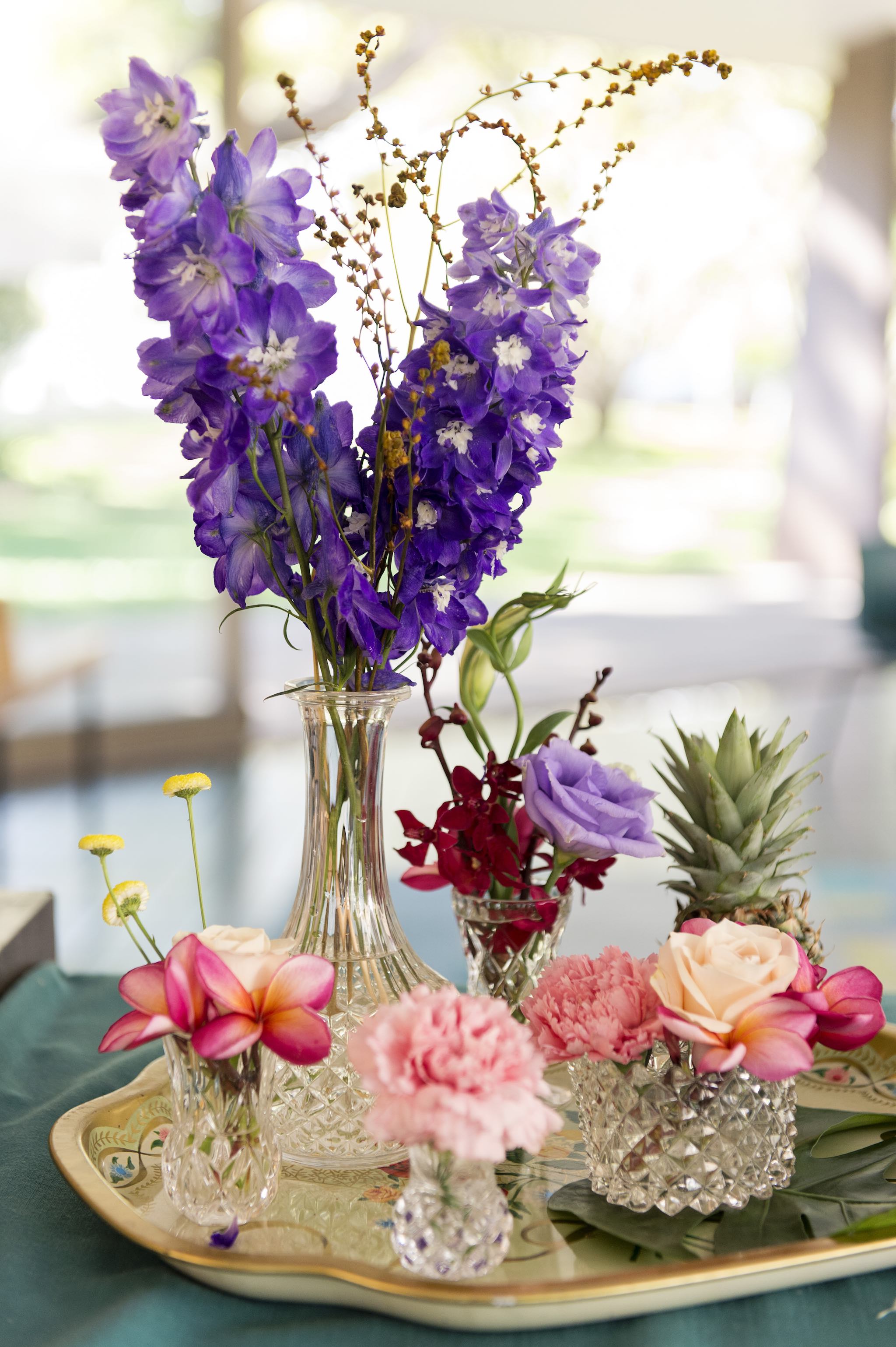 crystal vases topped with delphiniums, roses and pineapples