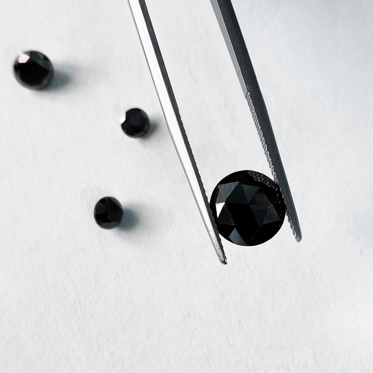 A black diamond being held by tweezers with other black diamonds around it.
