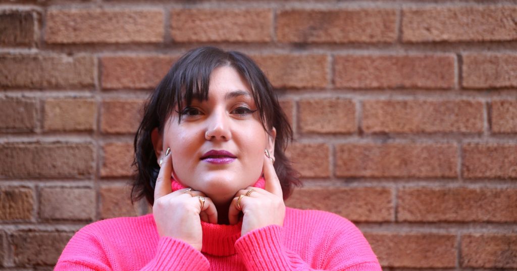 A woman has her two pointer fingers on her cheek showing off her rings.