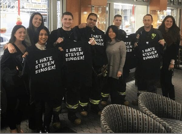 A group of customers and workers holding up "I Hate Steven Singer" shirts.