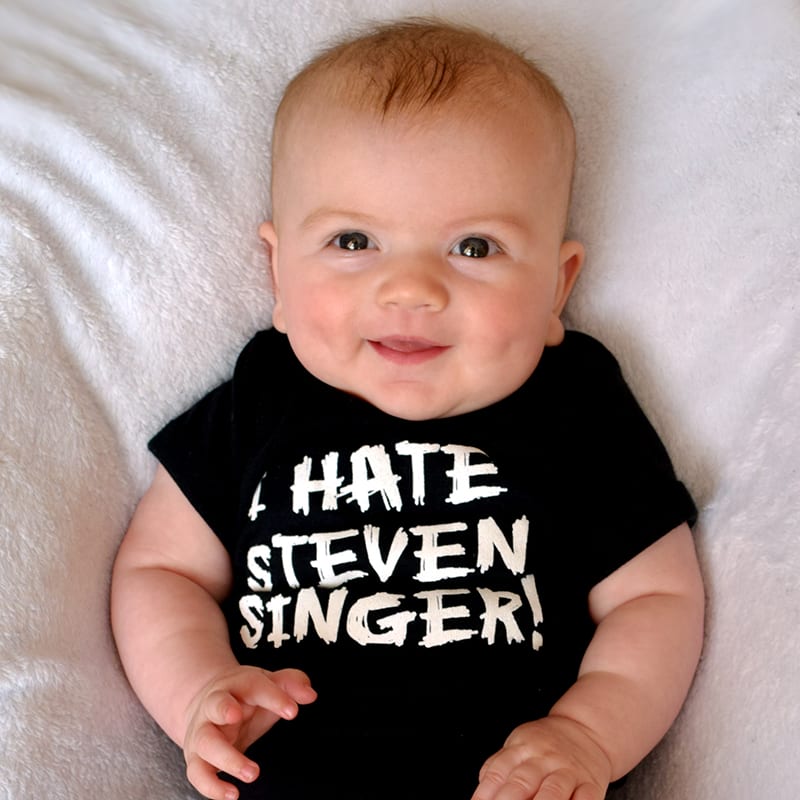 A smiling blonde baby in a "I Hate Steven Singer!" shirt.