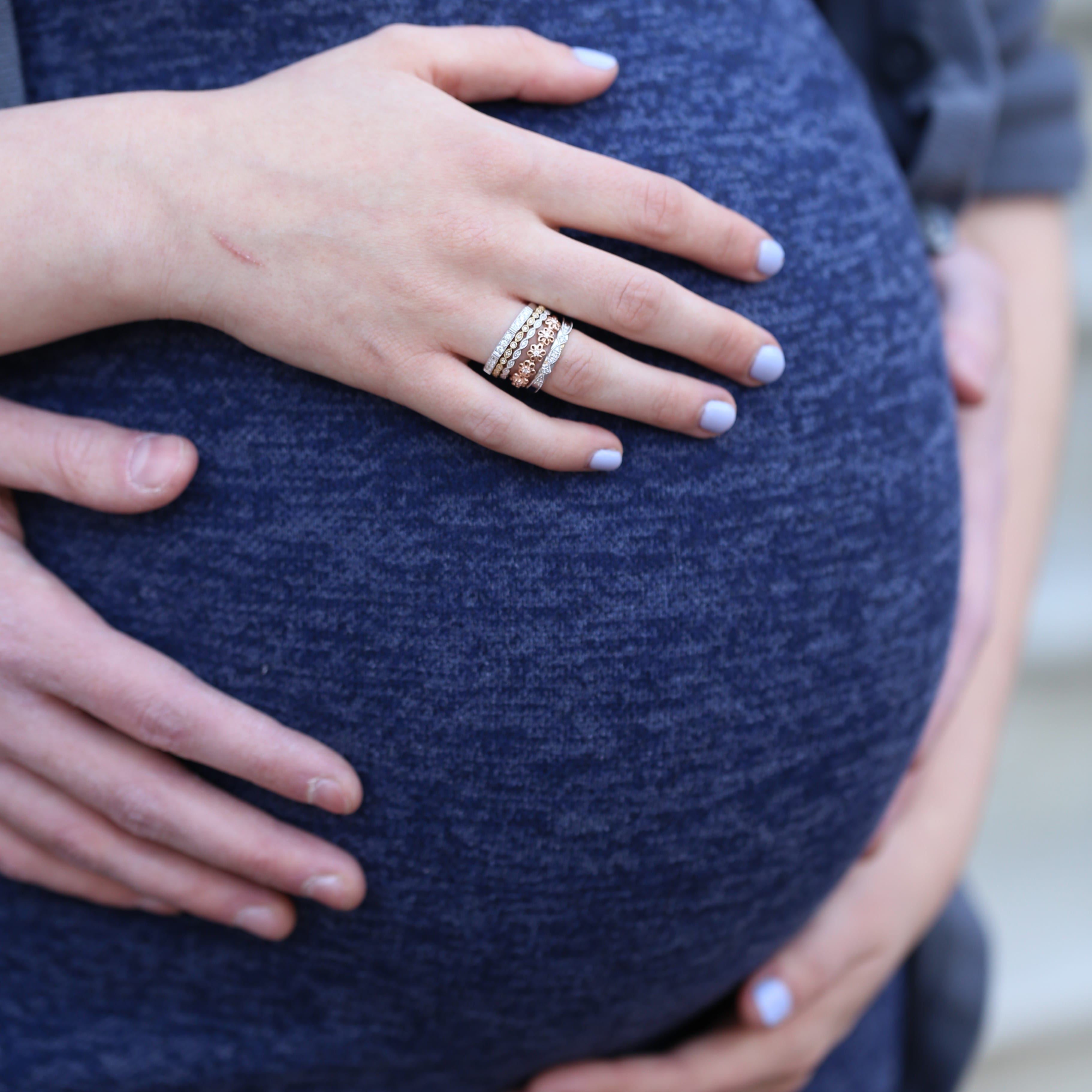 A pregnant mothers belly with her hands over it.