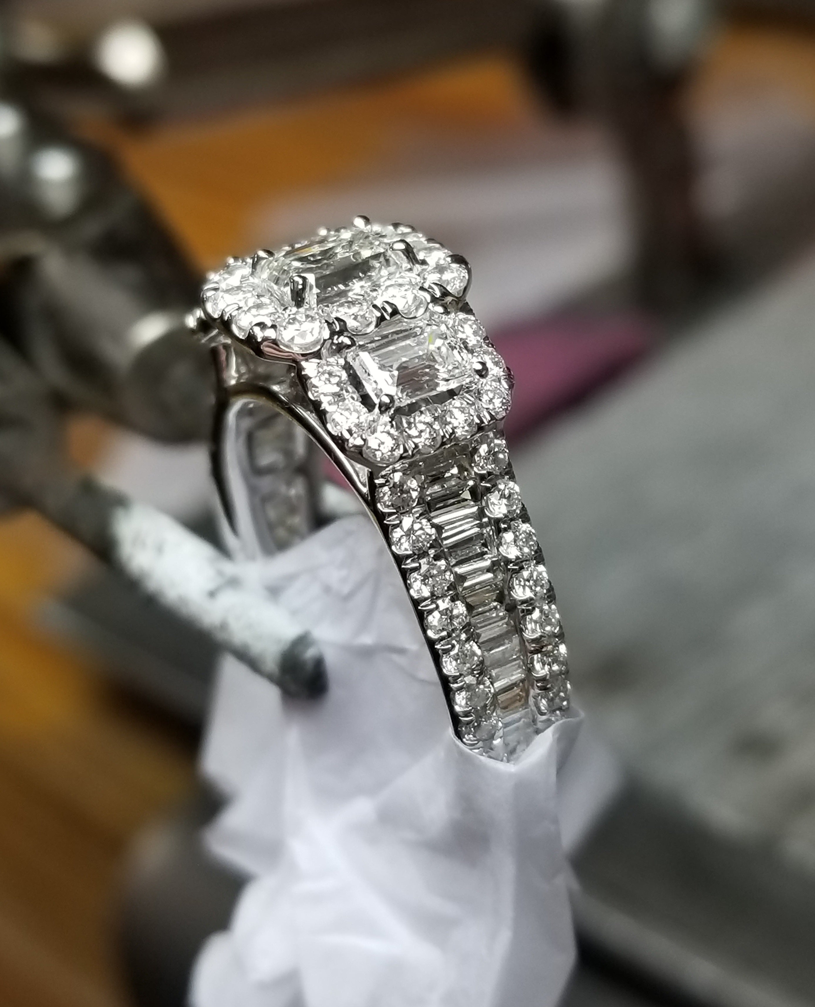 Tweezers holding up a beautiful step cut diamond ring with multiple stones.