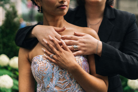 A woman in a suit hugging a woman in a dress from behind.