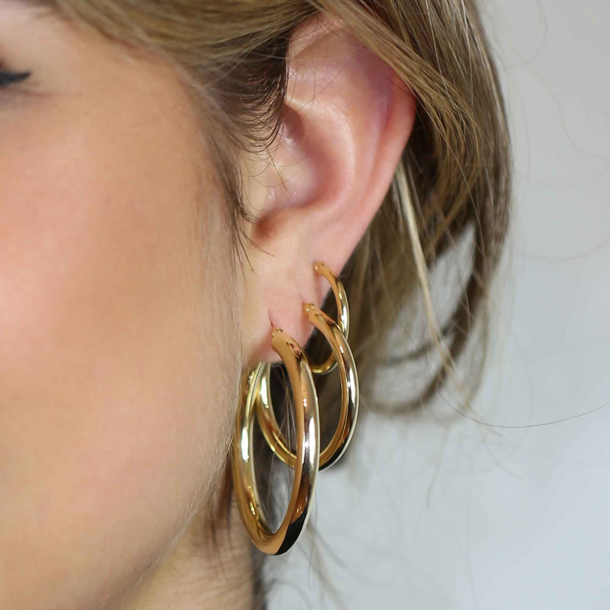 Three different size yellow gold hoop earrings in one ear