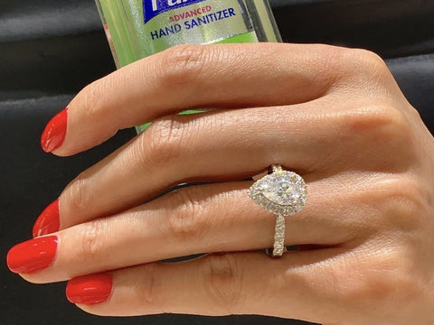 A woman with a pear shaped diamond ring holding hand sanitizer.
