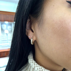 A woman with black hair wearing a pair of Steven Singer Jewelers Classic Channel Diamond Huggie Hoop earrings