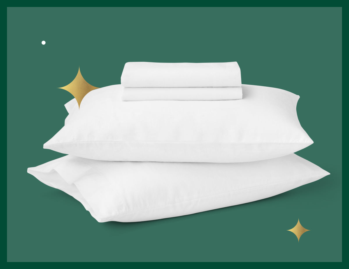 Two Tuft & Needle pillows stacked on top of each other with linen sheets folded on top of them. Picture has a green background with gold stars.