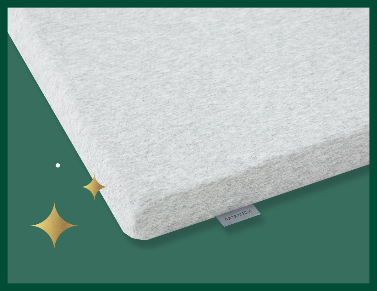 Corner of a Tuft & Needle mattress topper. Picture has a green background with gold stars.